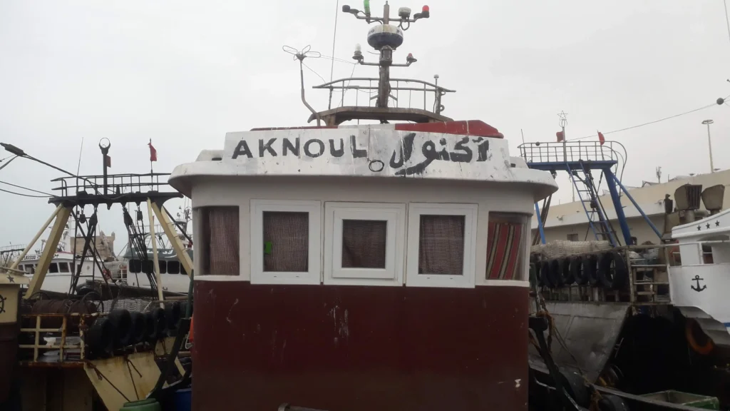 Photo du bateau de pêche traditionnel Aknoul en mer à Essaouira, capturant des poissons frais pour le Restaurant Café El Azzam.